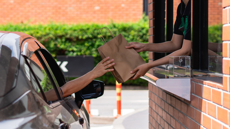 Fast food employee handing a bag of food to customer in drive-thru