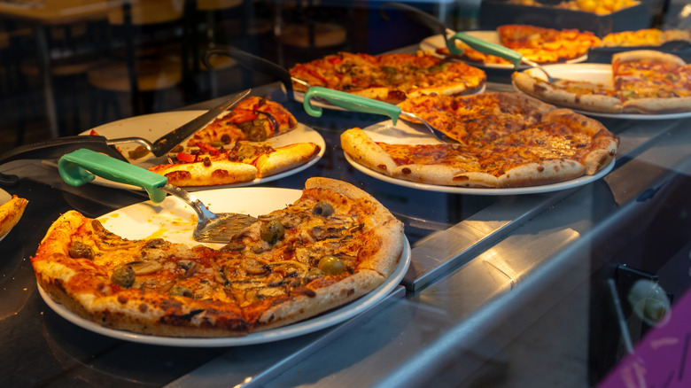 Different pizzas lined up at a pizza buffet
