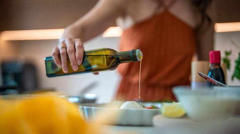 Person pouring olive oil onto a dish of food