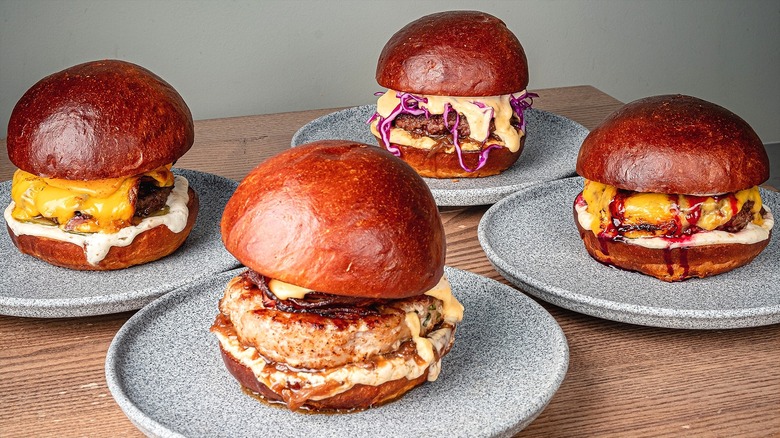 Four burgers with various toppings, melted cheese, and condiments on gray-speckled plates