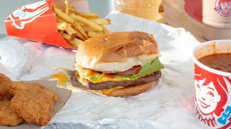 A Wendy's burger with melted cheese surrounded by other Wendy's classic, including nuggets, fries, and chili.