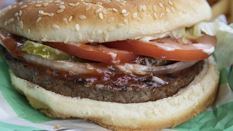 A close up of a hearty Burger King whopper with tomatoes, ketchup, pickles, and lettuce.
