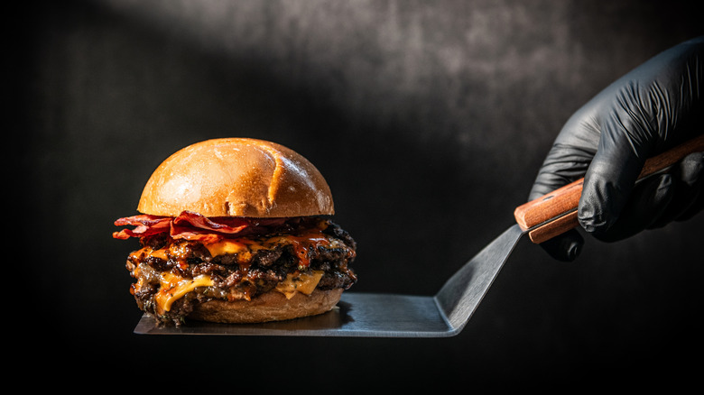A black gloved hand holds a burger on a spatula