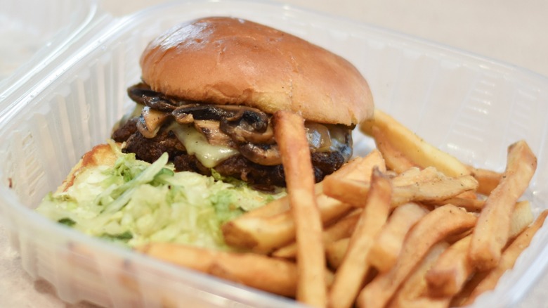 A Chili's Mushroom Swiss burger in a clear container with fries on a white countertop