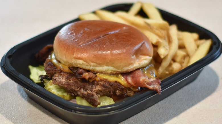 An Applebee's bacon burger in a black container with fries on a white countertop