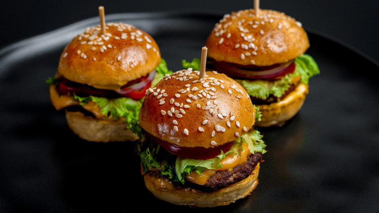 three mini cheeseburgers with lettuce on a black plate