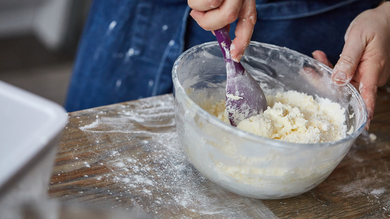 An illustrative image showing an individual mixing a cake batter in a bowl with a spoon.