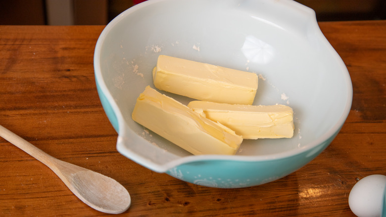 An illustrative image showing sticks of butter in a mixing bowl with a spoon on the side.