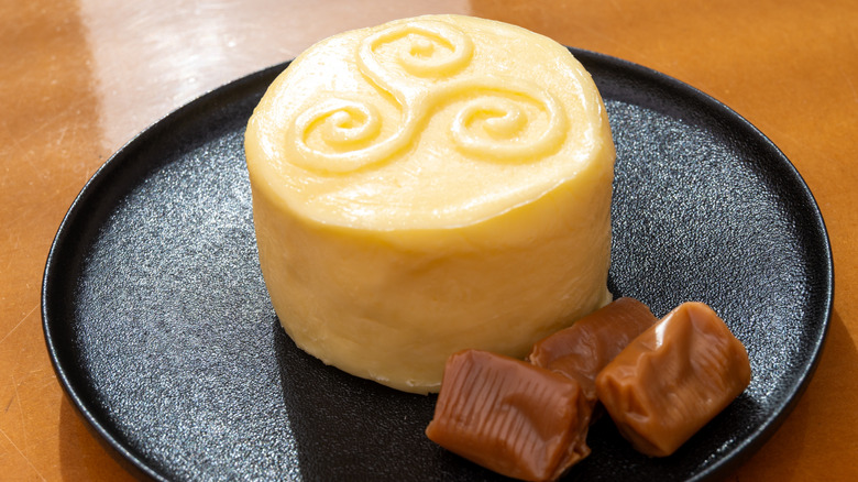 A round piece of butter with a decorative top on a plate with three caramels