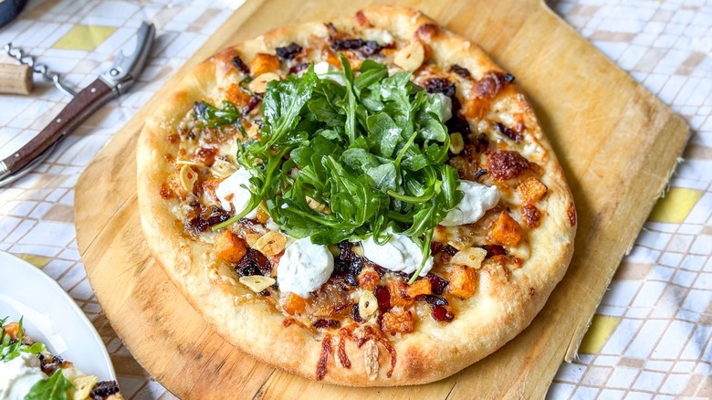 Butternut squash and maple bacon pizza on pizza peel on tablecloth