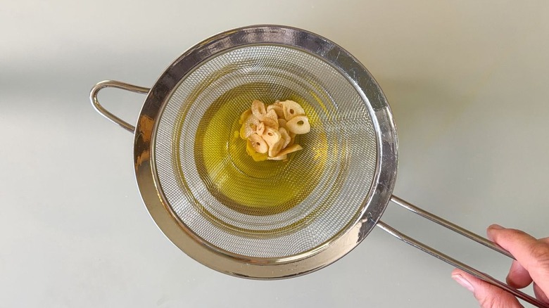 Straining garlic oil through fine mesh strainer holding garlic chips