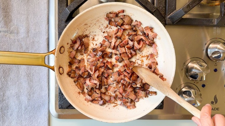 Stirring bacon lardons in skillet with wooden spoon