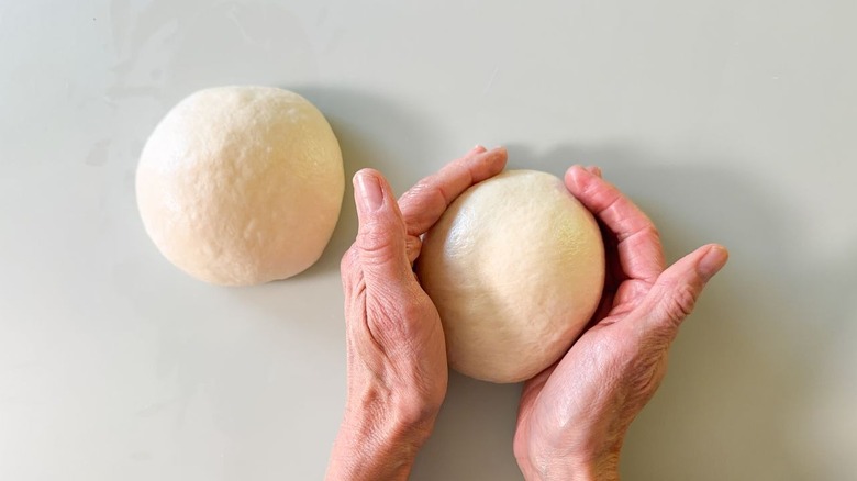 Shaping pizza dough into 2 balls on countertop