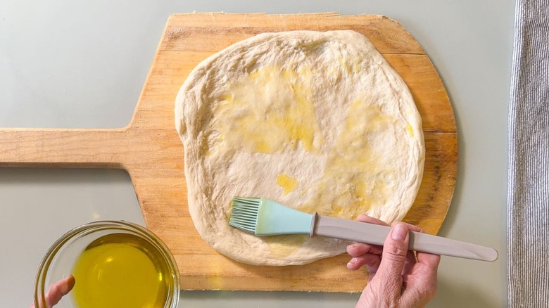 Applying garlic oil to unbaked pizza crust with pastry brush