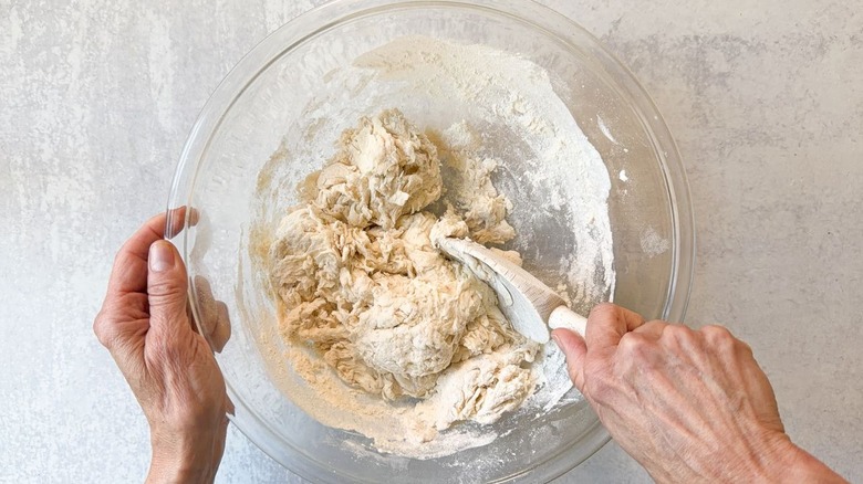Mixing pizza dough with wooden spoon in glass bowl