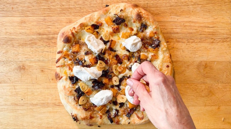 Sprinkling fried garlic chips onto baked butternut squash and maple bacon pizza
