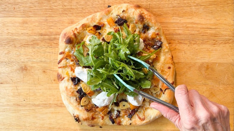 Piling dressed arugula onto baked butternut squash and maple bacon pizza