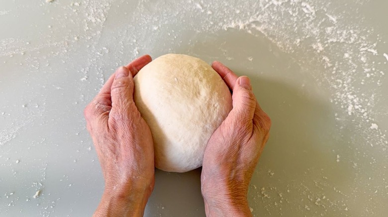 Shaping pizza dough into a ball by hand on a countertop