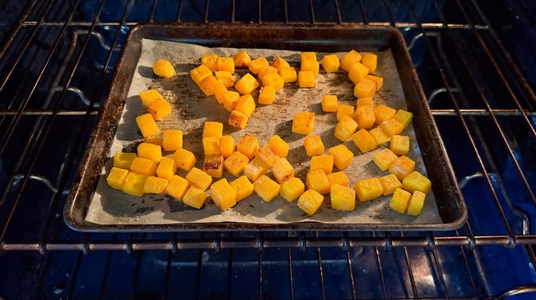 Butternut squash cubes roasting on parchment-lined baking sheet in oven