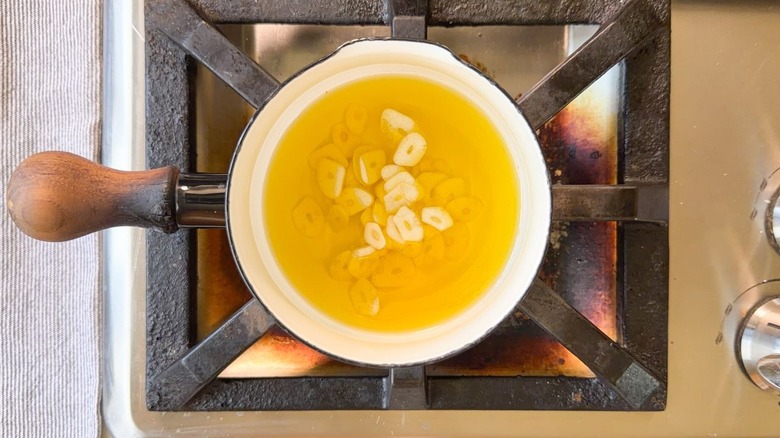 Slivers of garlic in olive oil in small saucepan on stovetop