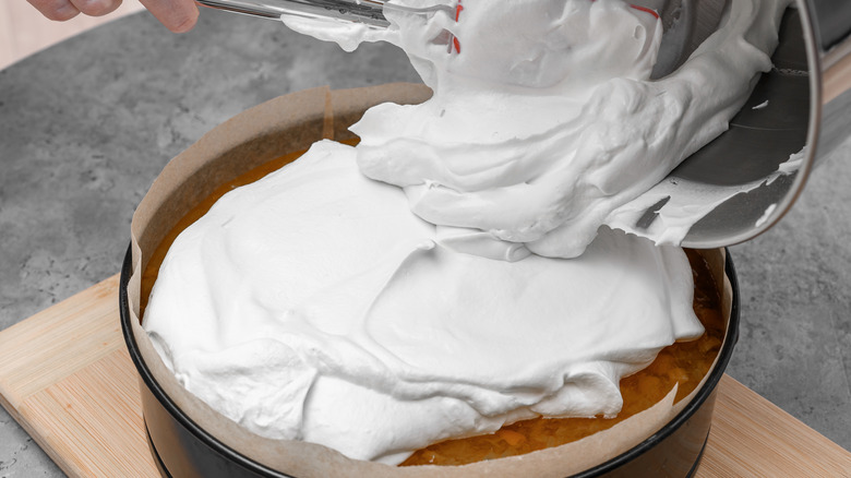 Person pouring frosting on a cake from a bowl.