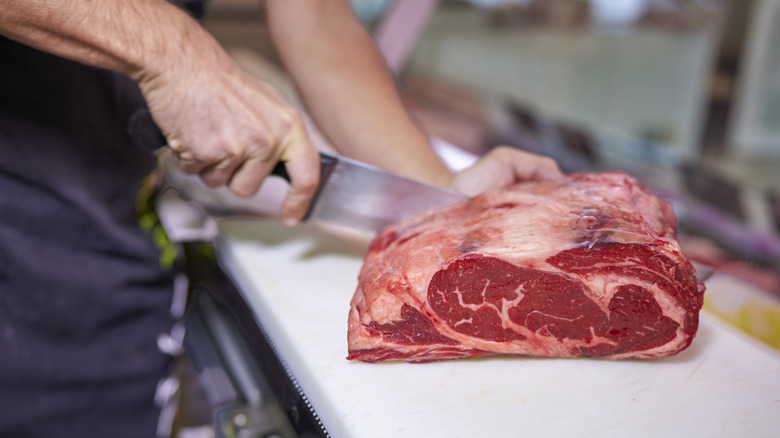 A butcher portioning steaks from a ribeye roast.