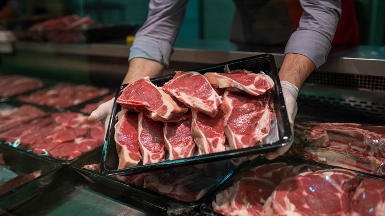 A butcher holding portions of steak behind a counter.