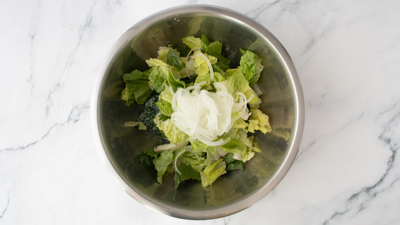 A large bowl of salad greens and thin slices of onion