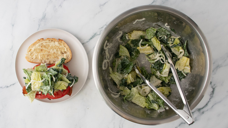 Bread slices topped with bacon, white sardines, tomato slices and caesar salad