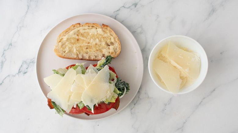 A stacked caesar BLT sandwich topped with shaved parmesan
