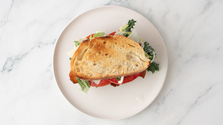 A caesar BLT sandwich on a white plate
