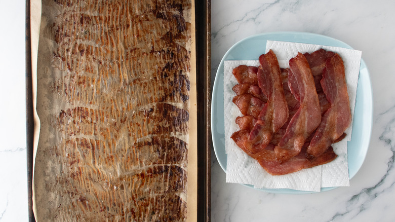 Bacon removed from a baking sheet and placed on a paper towel-lined plate