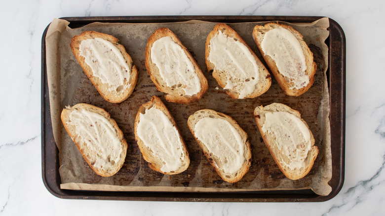 Toasted bread slices on a baking sheet spread with creamy dressing