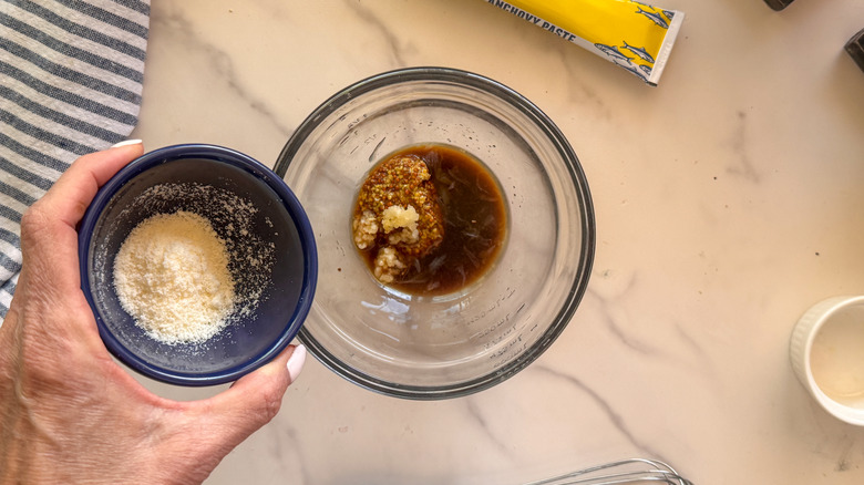 hand adding parmesan to bowl