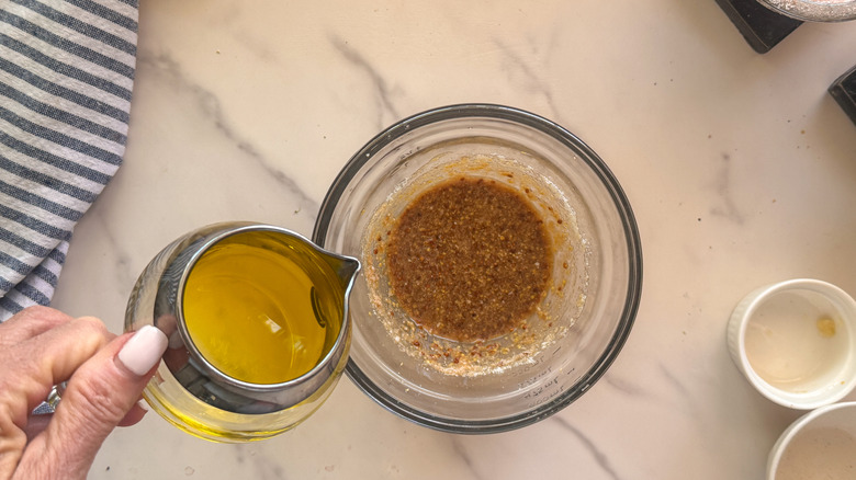 hand adding olive oil to bowl