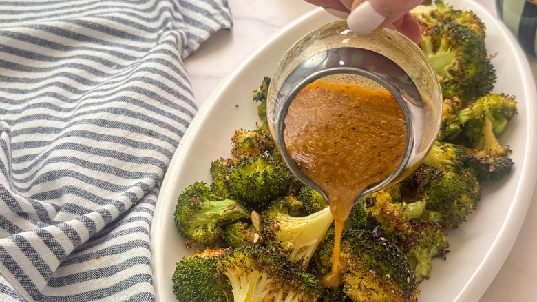 hand pouring dressing onto broccoli