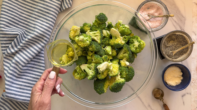 hand adding oil to bowl with broccoli