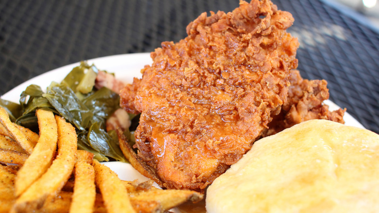 Southern style meal with fried chicken, collard greens with bacon, French fries, and a biscuit.