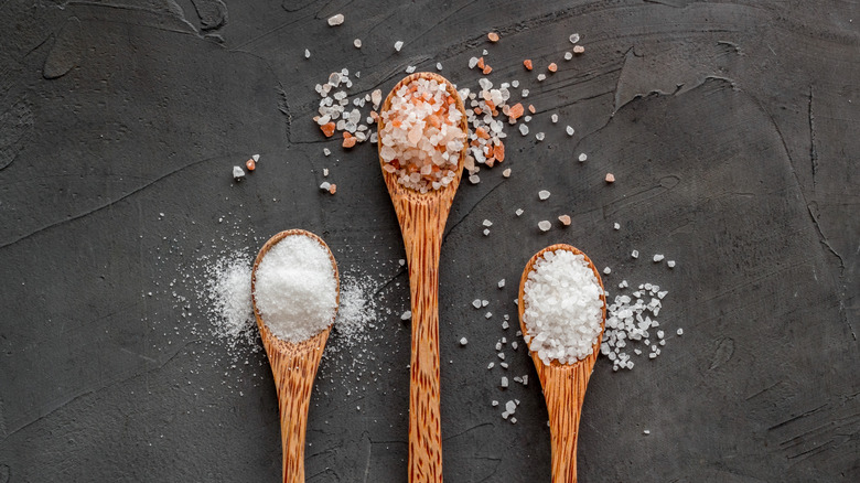Flat lay of sea salt in wooden spoons on a grey background.