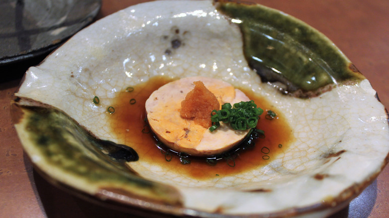 Monkfish garnished with scallions, momiji oroshi, and ponzu sauce in a green and light gray ceramic dish