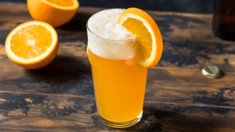 A pint of beer on a wooden table with an orange garnish.