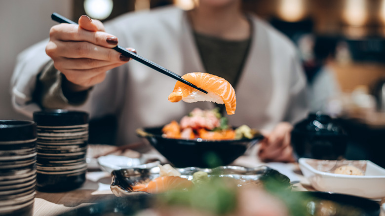 A manicured hand holding chopsticks, lifting a piece of salmon sushi