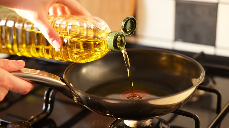Woman pouring oil into frying pan on stove, closeup