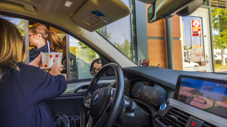A woman accepting McDonald's soft drinks at a drive-thru window