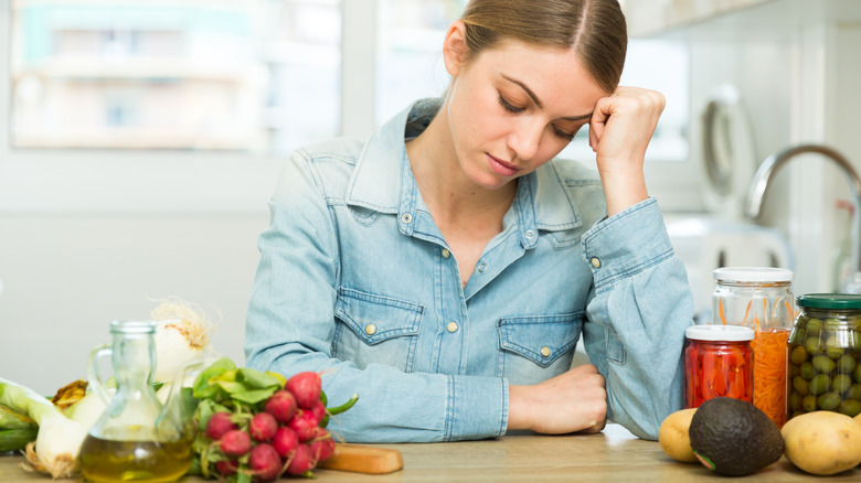a woman having a migraine at a kitchen counter surrounded by produce