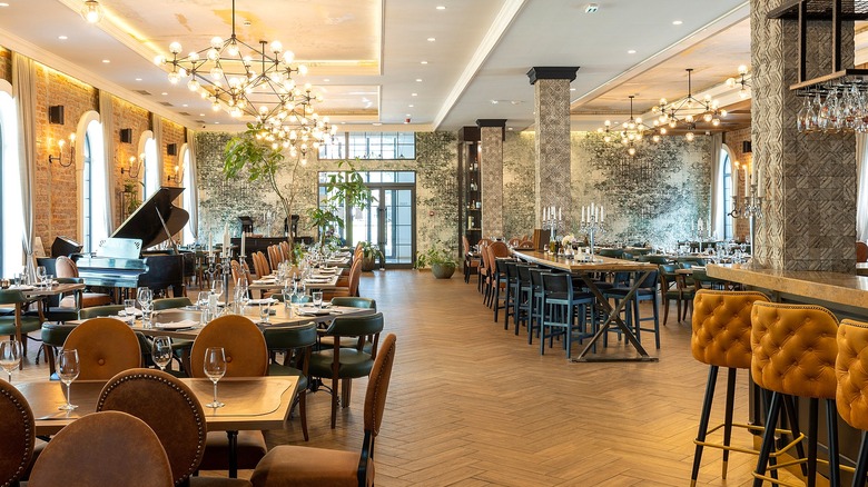 Empty upscale restaurant with modern lighting, cushioned sheets, and a grand piano