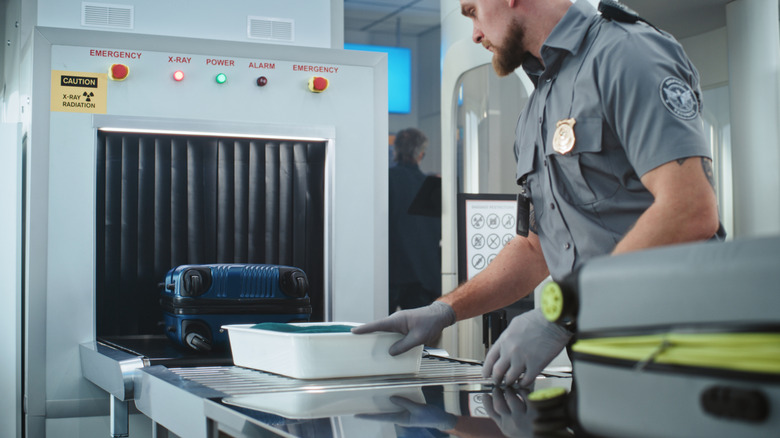 A TSA agent pushing items through an x-ray machine at an airport security checkpoint.
