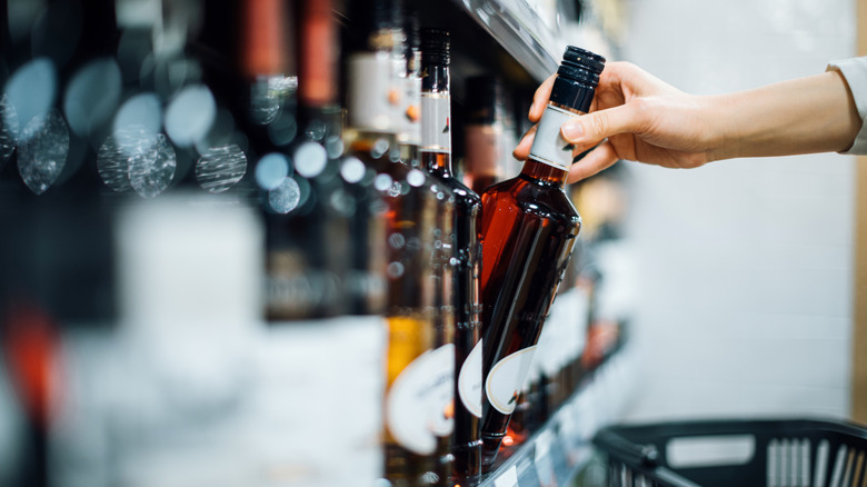 Hand picking up a bottle of liquor off a shelf