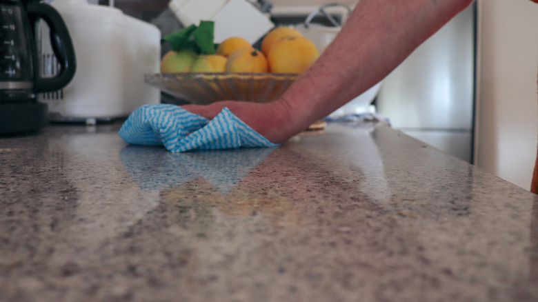 A person's hand is seen cleaning a countertop with a cloth.