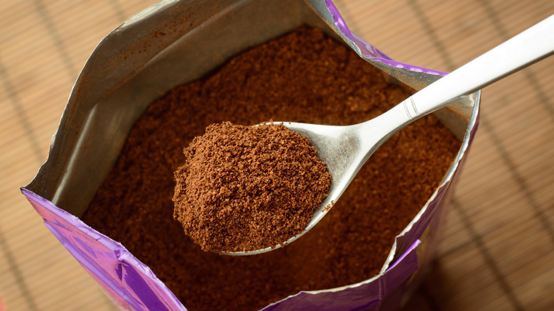 A spoon scooping ground coffee from a bag.